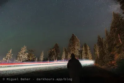 A stargazer silhouetted against car light trails on Mt Ashland, Oregon