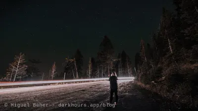 A stargazer standing in the road with car light trails behind on Mt Ashland, Oregon